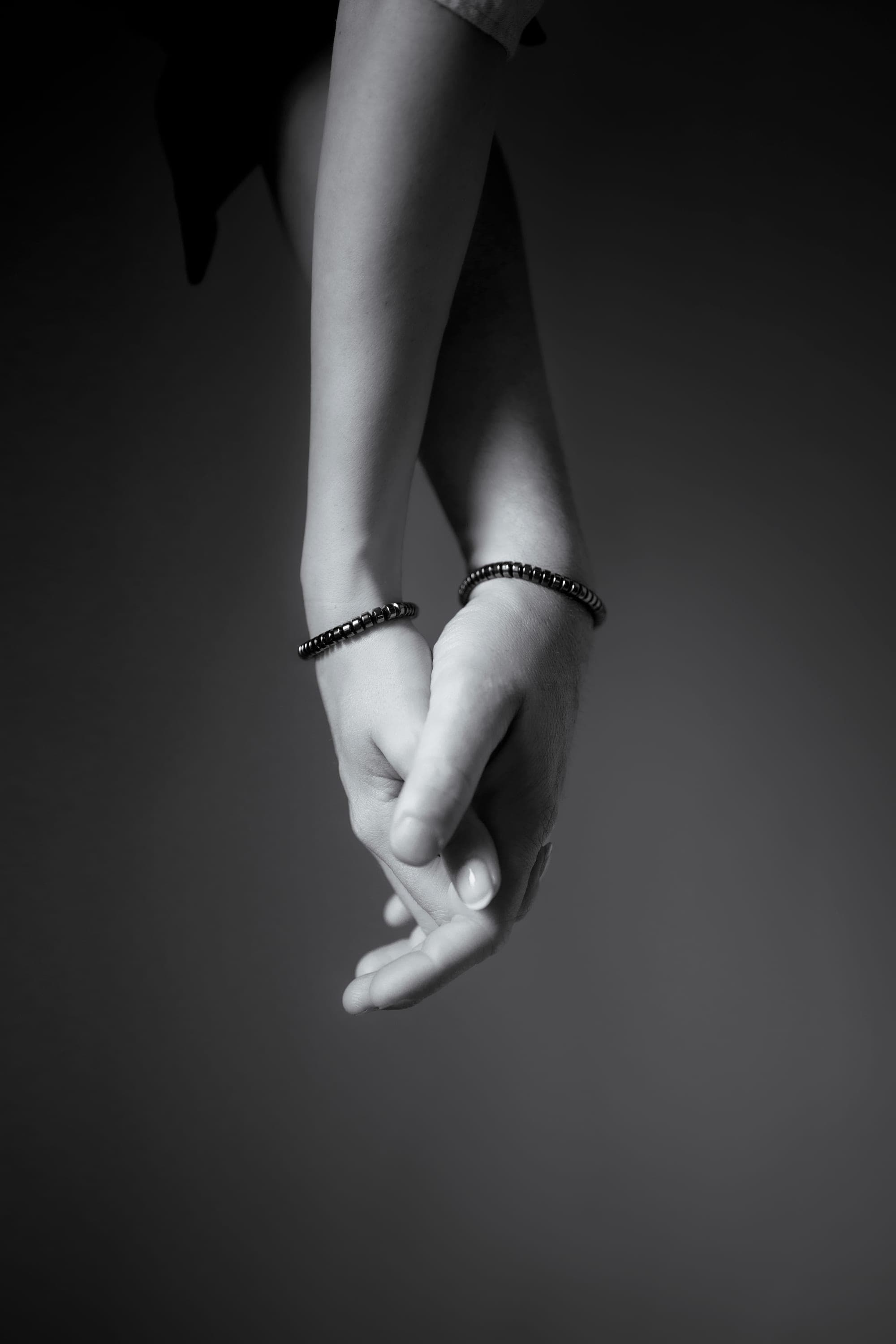 Two hands held loosely together, each wearing an IONISS hematite bracelet