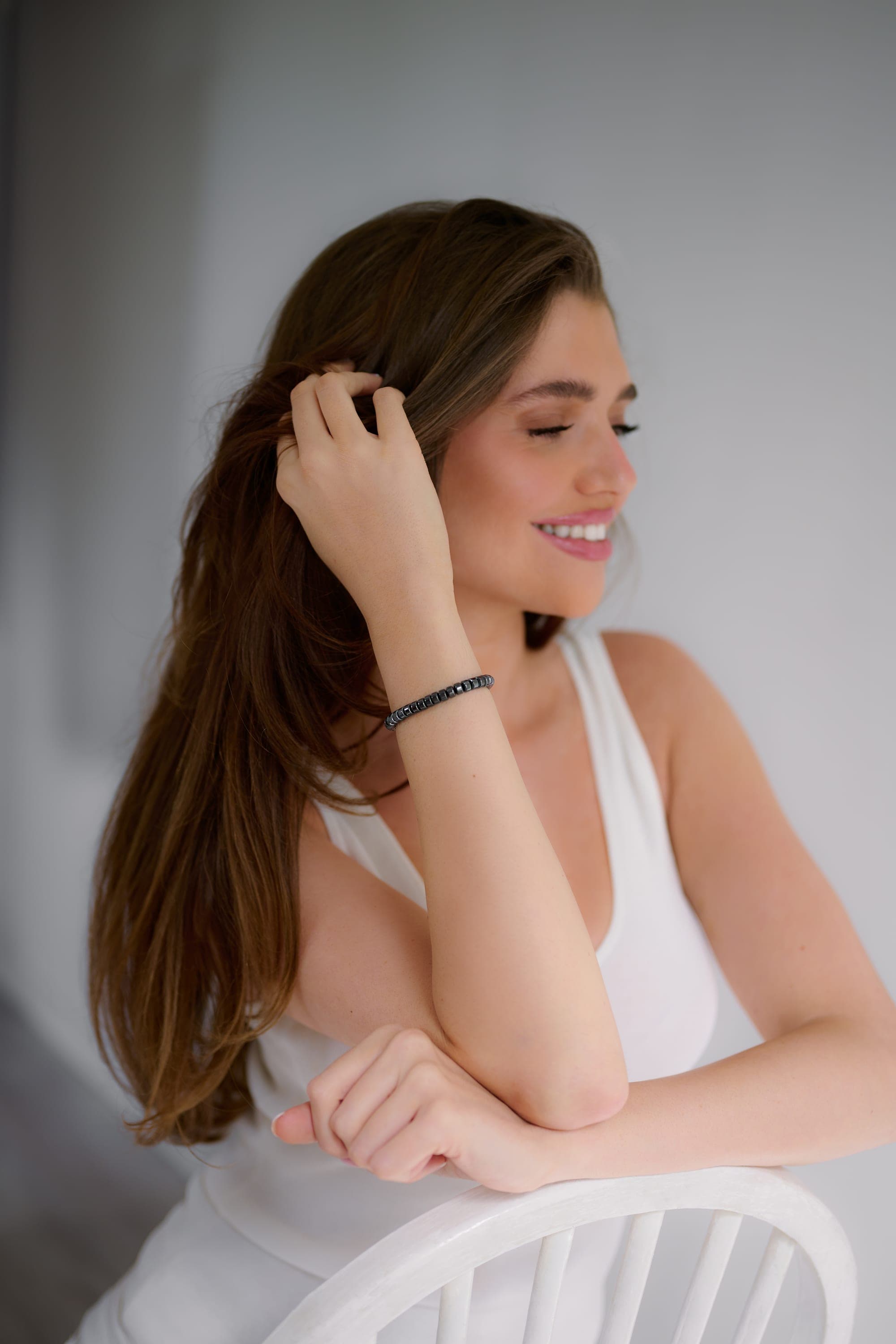 A woman seated in a white top, wearing the IONISS hematite bracelet on her wrist