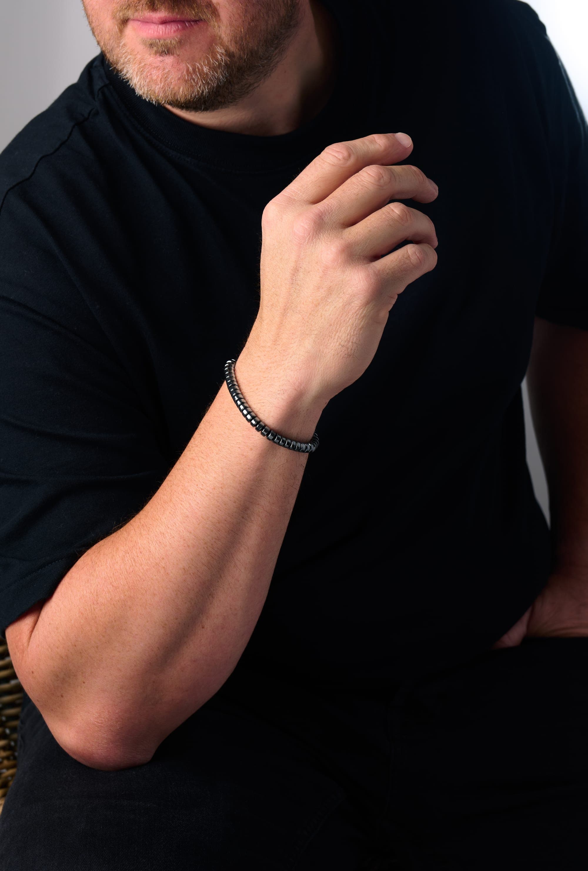 A man in a black t-shirt wearing the IONISS hematite bracelet on his wrist