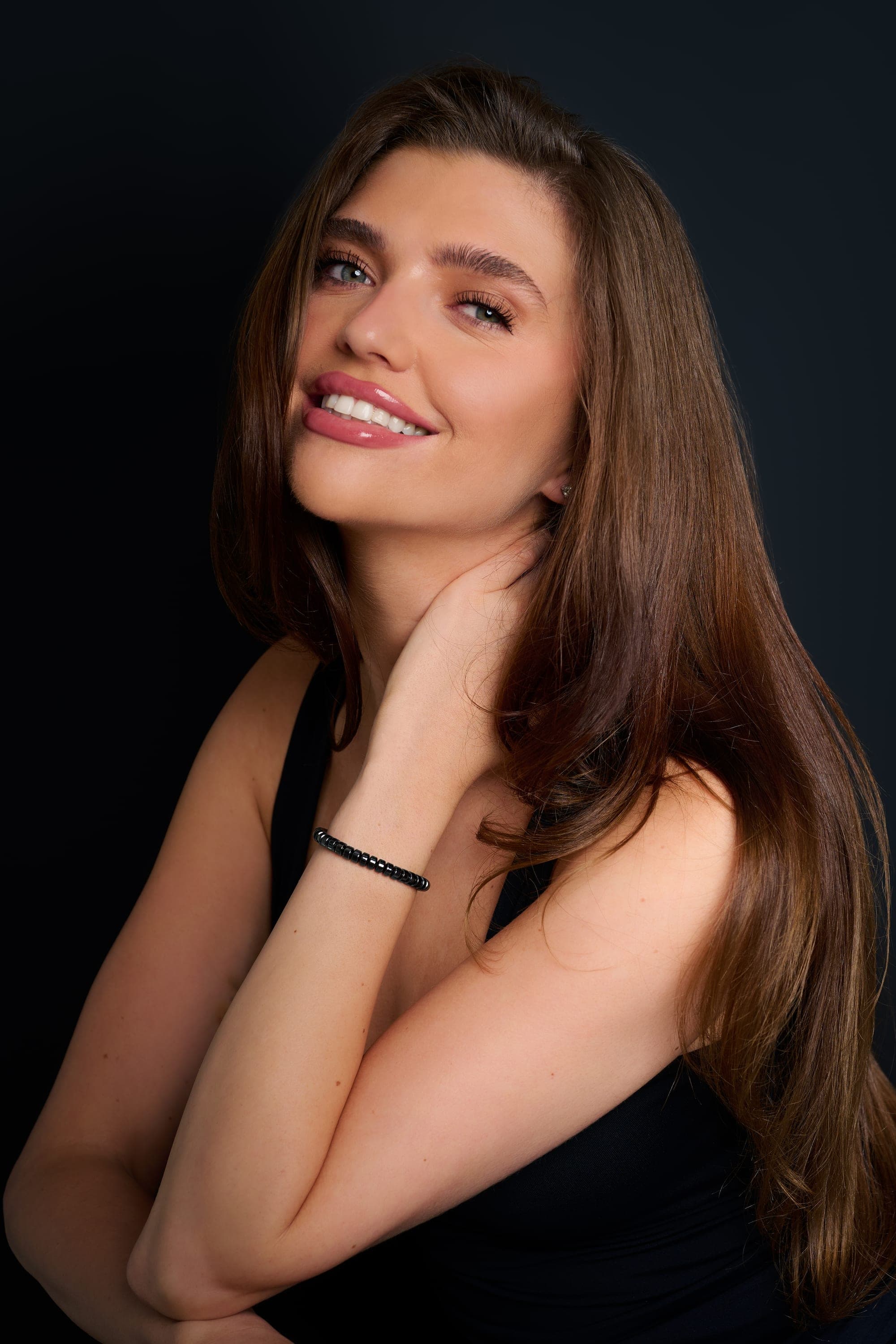 A woman against a dark background, the IONISS hematite bracelet visible on her wrist